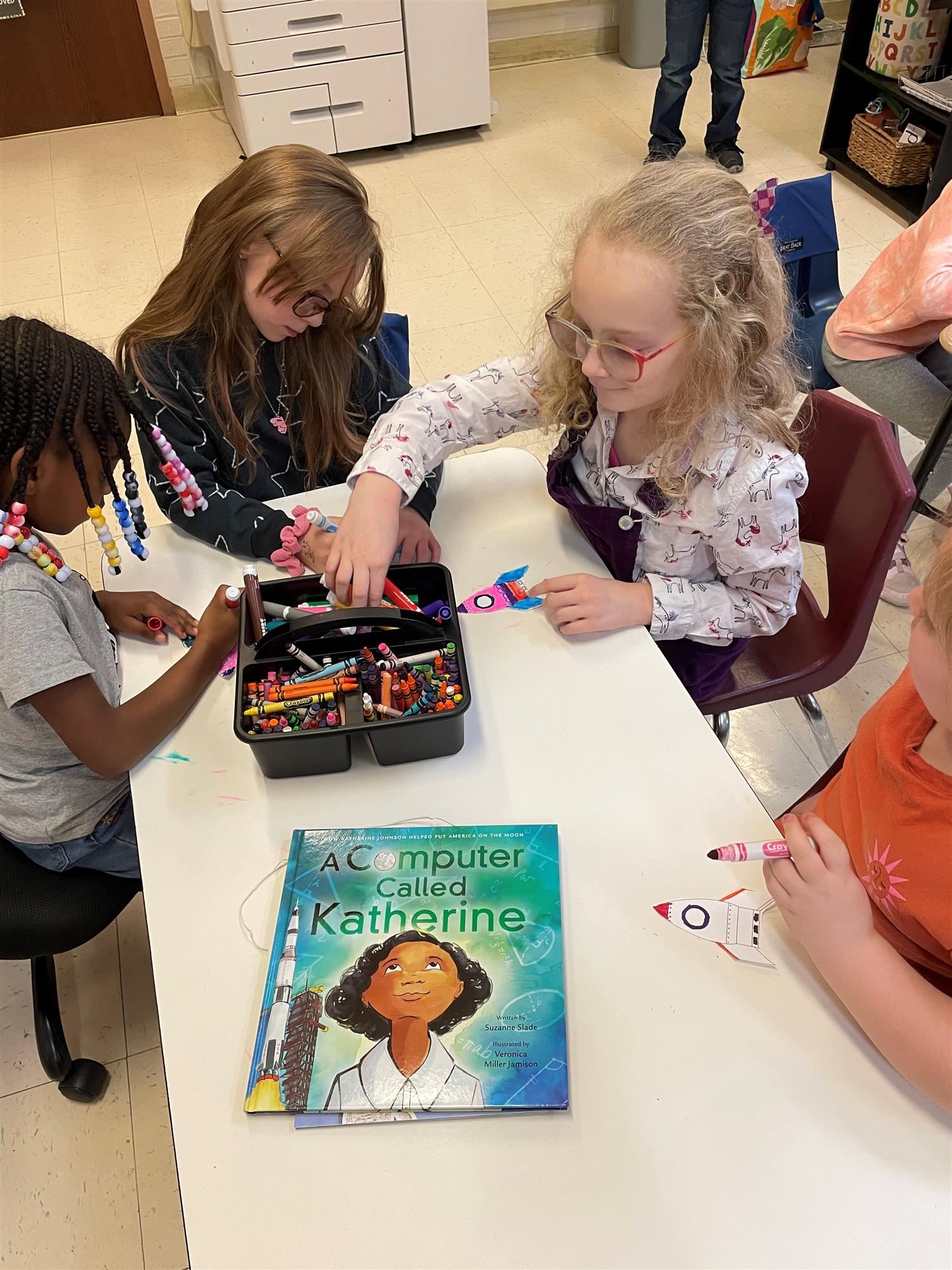 Photo of students gathered around a table coloring rocketships.